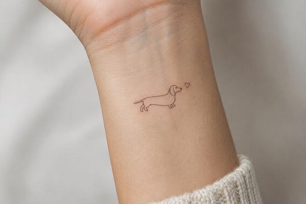 Kleines, minimalistisches Dackel‑Tattoo im feinen Linienstil am inneren Handgelenk