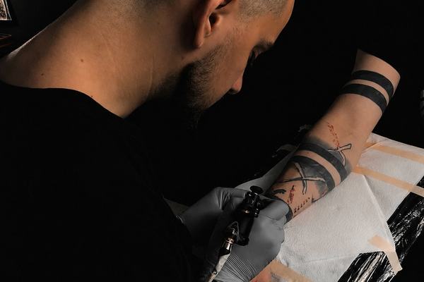 Tätowierer sticht ein Tattoo am Unterarm