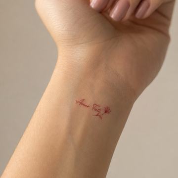 Minimalist red-ink “Amor Fati” Latin script tattoo with a tiny rose