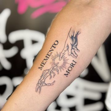 Unterarmtattoo in Schwarzgrau: vertikaler Schriftzug MEMENTO MORI neben 
