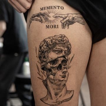 Schwarzgraues Oberschenkel‑Tattoo mit dem Schriftzug „MEMENTO MORI“