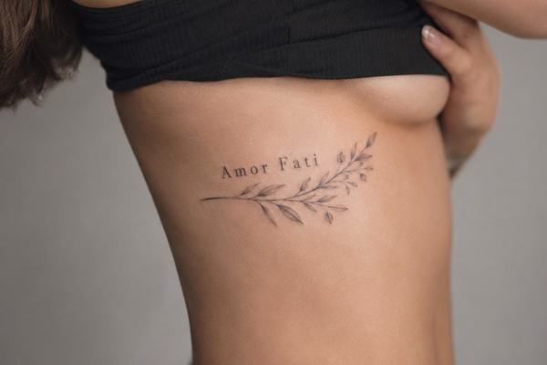 Seitliche Ansicht eines Oberkörpers mit kleinem „Amor Fati“-Tattoo