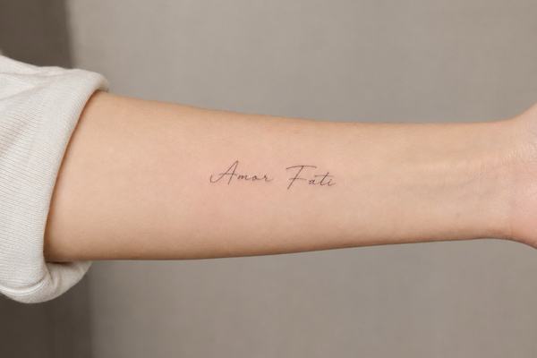 Unterarm mit kleinem, minimalistischen Script-Tattoo „Amor Fati“ 